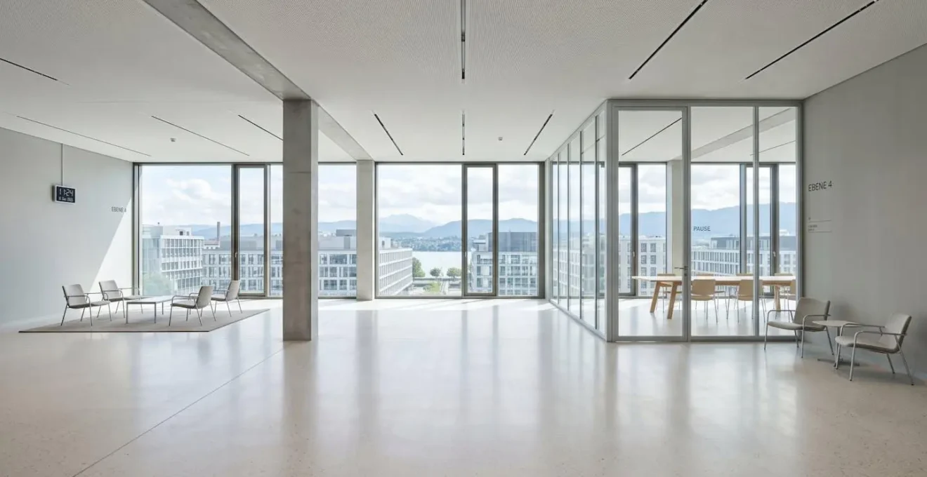 Weitwinkelaufnahme eines hellen, zeitgenössischen Büroraums mit grossen Fenstern und klaren Linien, menschenleer
